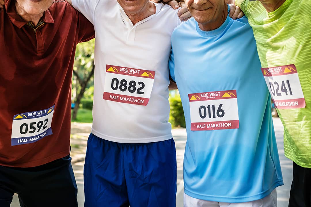 Elderly male runners grouped together with their marathon number tags on their shirts.